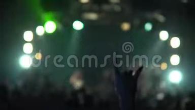 一个音乐音乐会上的女人举起了手。 一群欢笑的人站在鲜艳的舞台灯光前。 剪影式